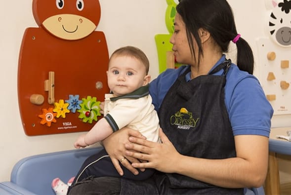 A woman in an apron holding a baby in a playroom.