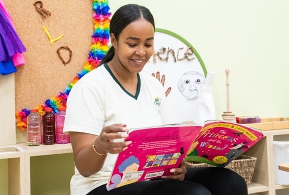 A woman reading a book in a children's room.