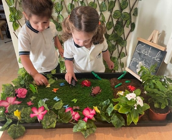 Two children playing with a tray of plants and flowers.