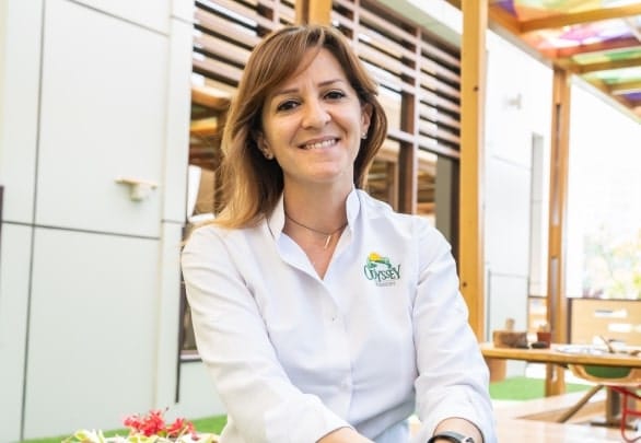 A woman in a white shirt smiling at a plate of food.