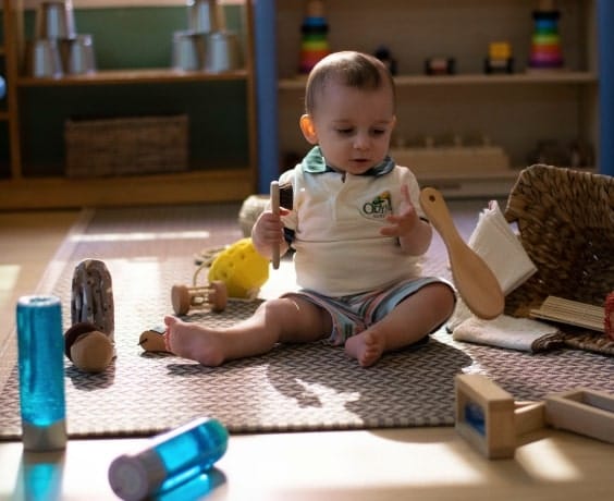 A baby sitting on the floor in a playroom.