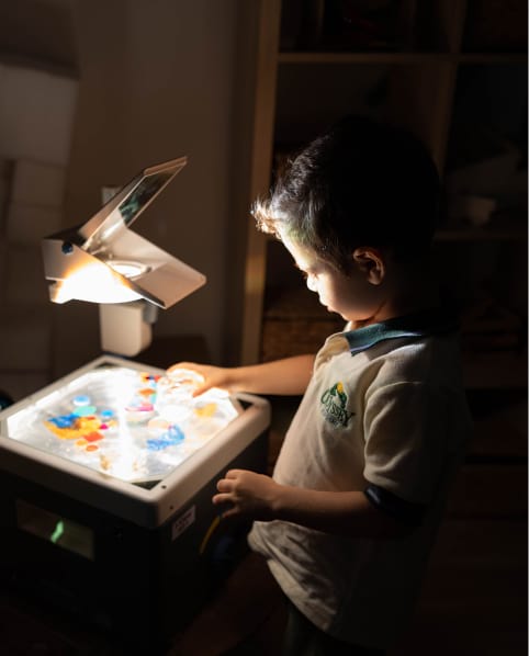A young boy playing with a light box in a dark room.
