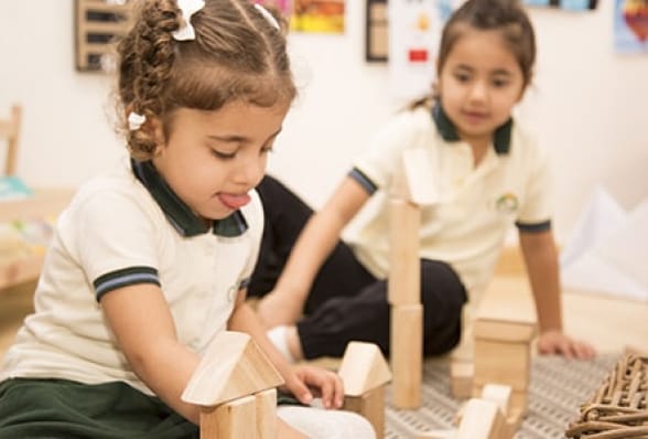 Two girls playing with wooden blocks in a classroom.